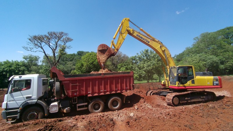 Escavadeira amarela carrega terra em caminhão durante obras de infraestrutura em Araras