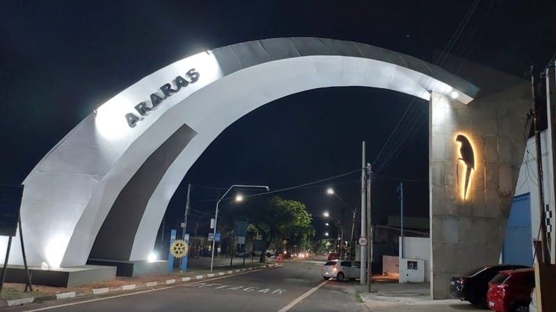 Portal de entrada de Araras SP iluminado à noite, com carros passando por baixo do arco