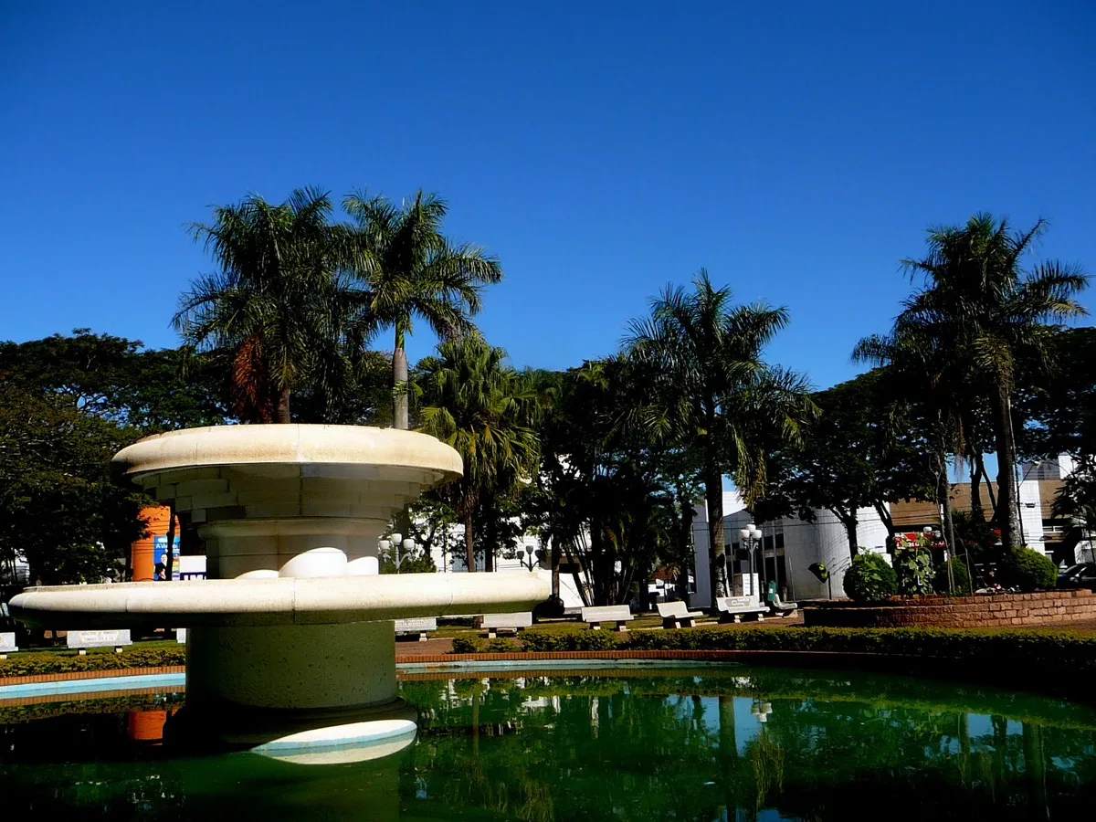 Fonte e jardim da praça central de Araras (SP) sob céu azul, com palmeiras ao fundo